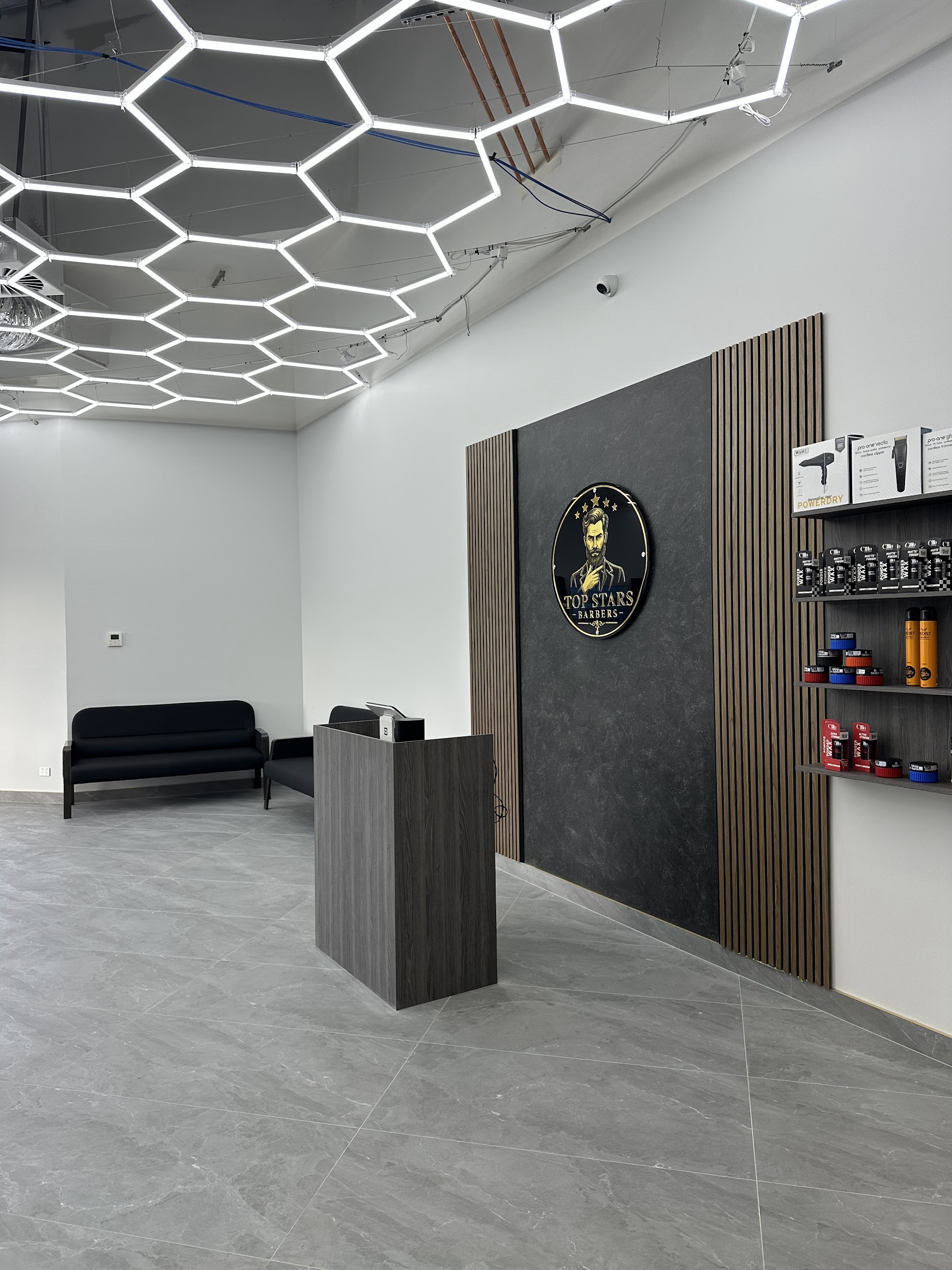 The front desk and waiting sofas beneath the shop's illuminated Top Stars Barbers sign
